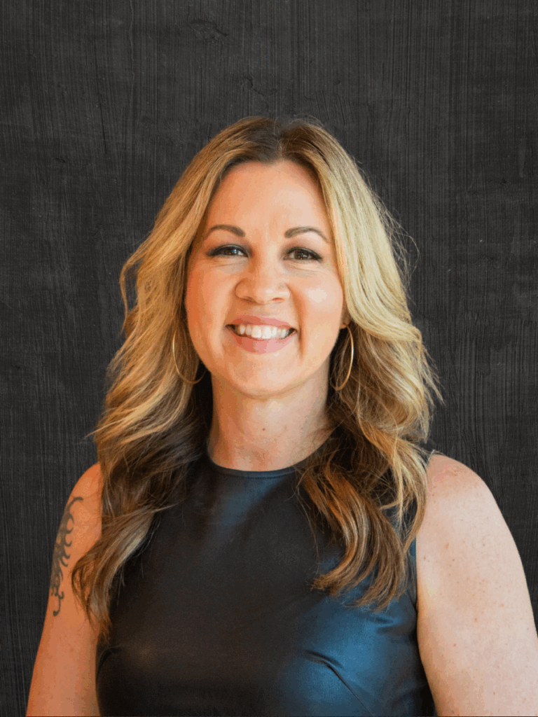 Wendy Berthiaume, co-owner of Front Room Hair Studio, smiling confidently, wearing a black top, showcasing her artistic hairstyling expertise.