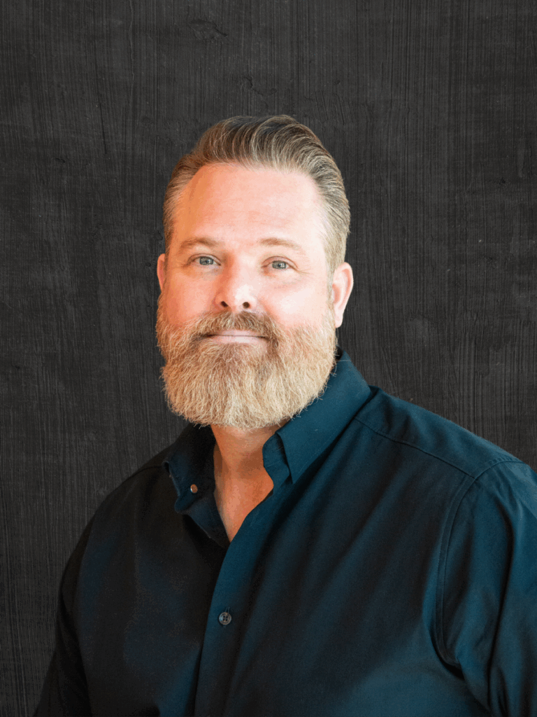 Co-owner of Front Room Hair Studio, smiling man with a beard in a dark shirt against a textured background.